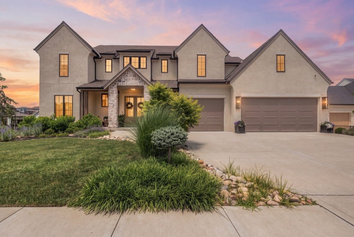 Stucco and stone two-story home at twilight with warm interior lights