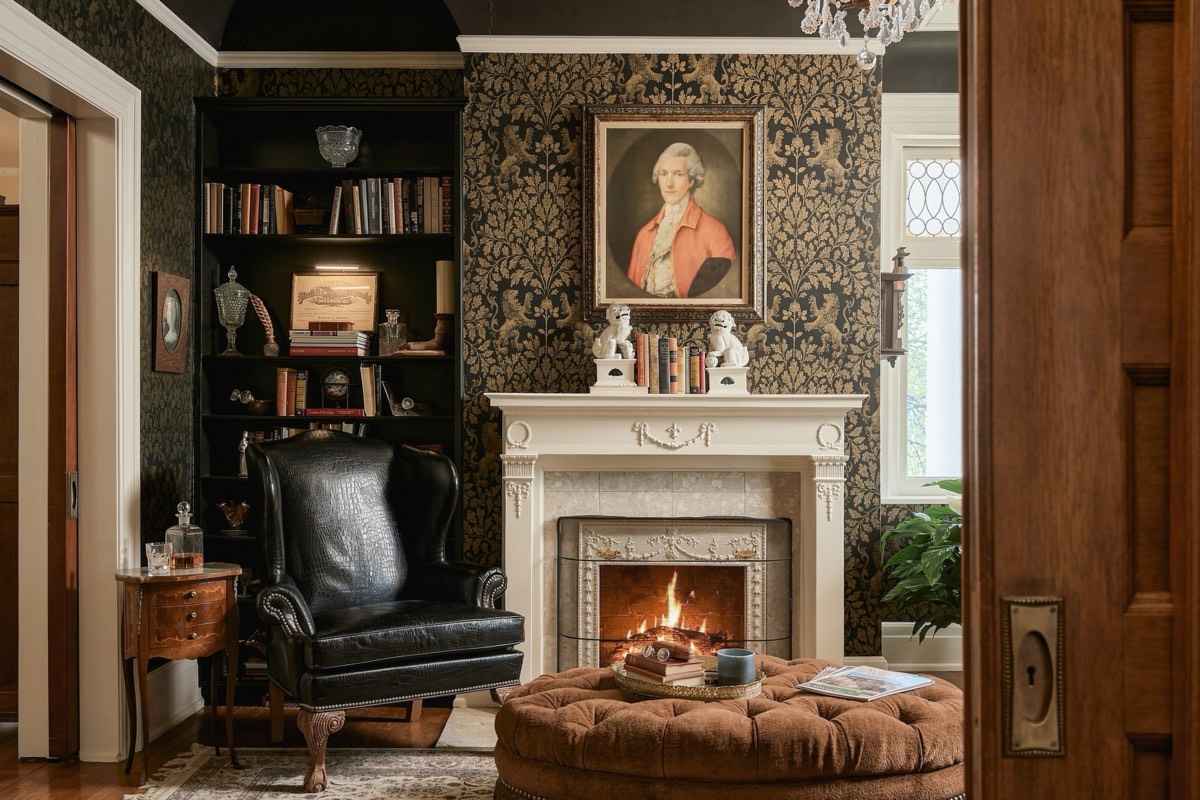 Historic study with patterned wallpaper, a leather wing chair and a lit fireplace