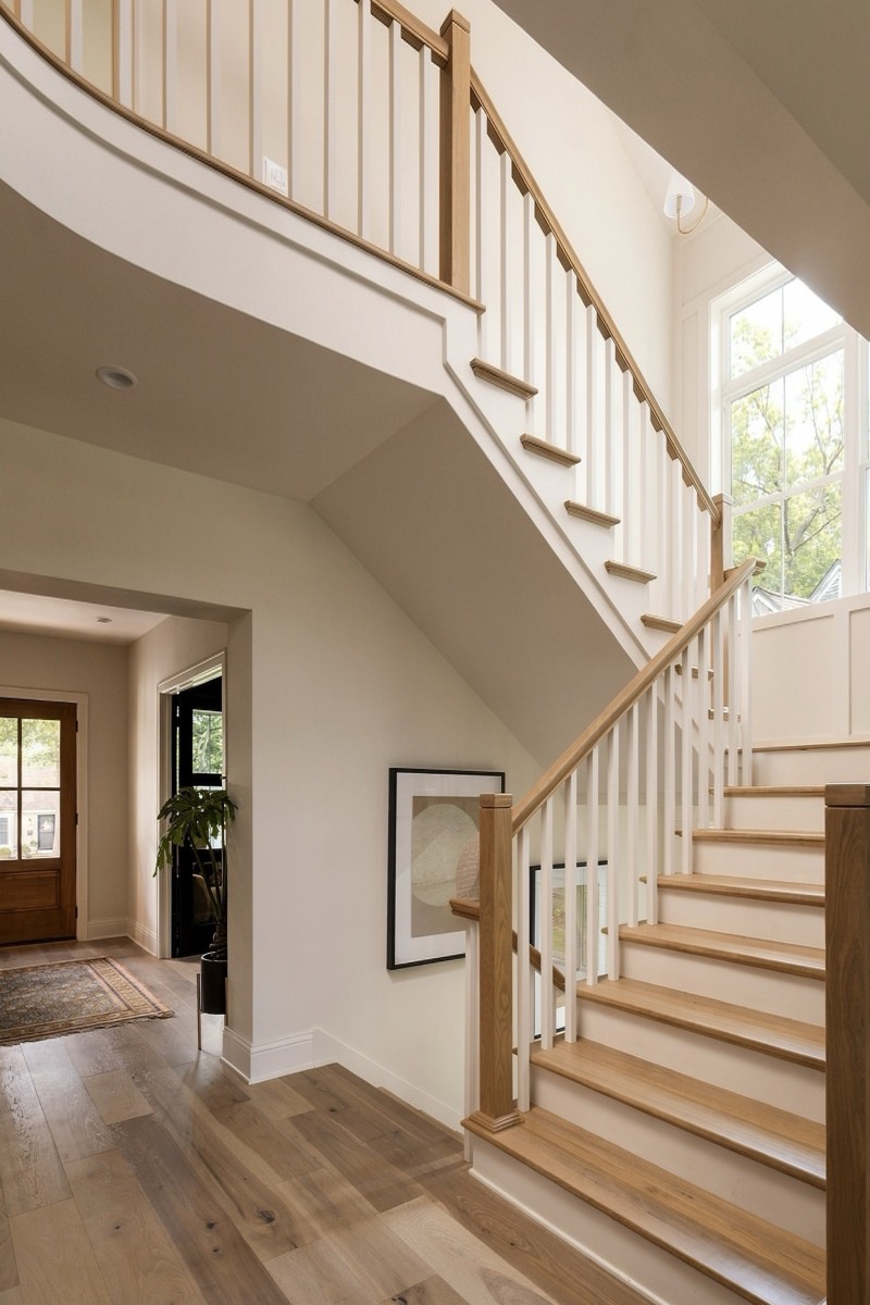White oak staircase rising from a light-filled entry