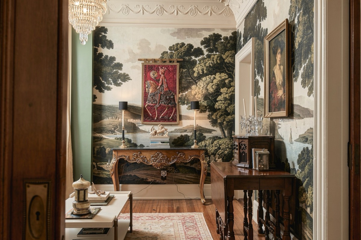 Entry hall lined with hand-painted scenic wallpaper and a crystal chandelier
