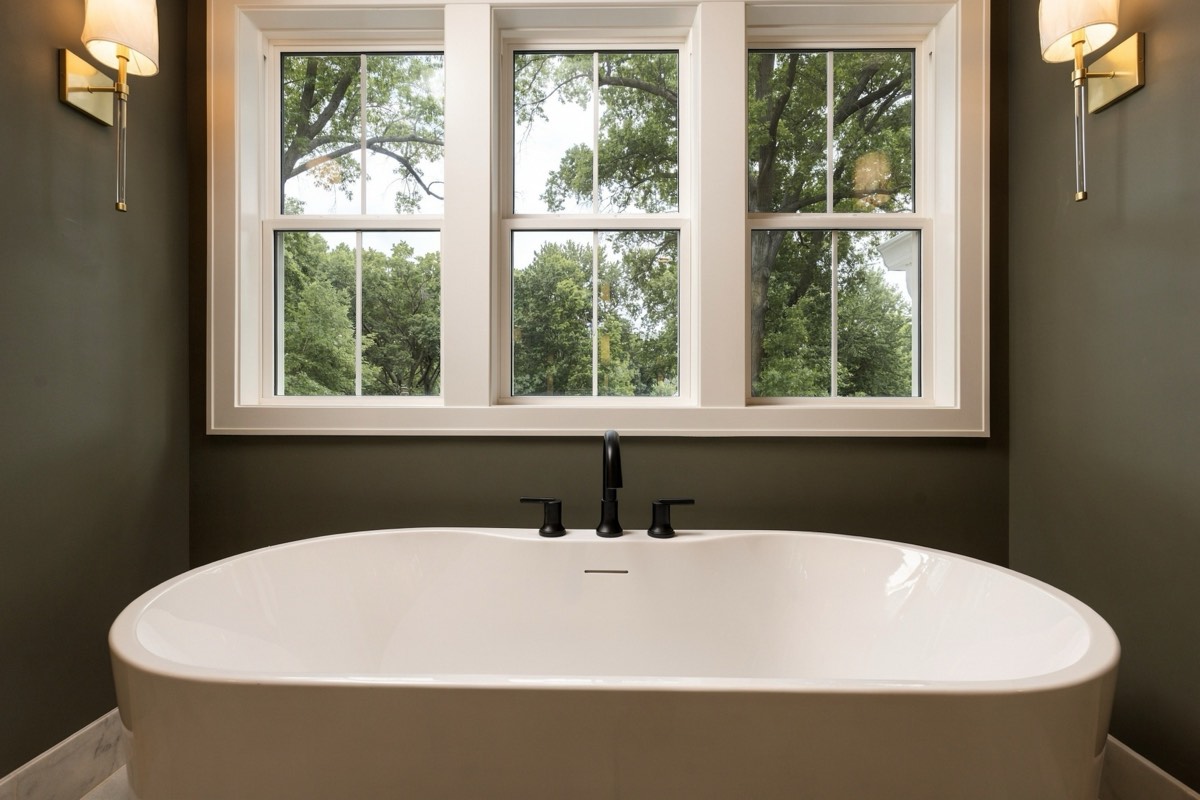 Olive bathroom with a freestanding tub beneath a triple window