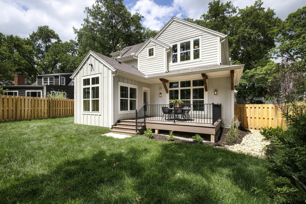 Rear of a white farmhouse with a covered deck and fenced lawn